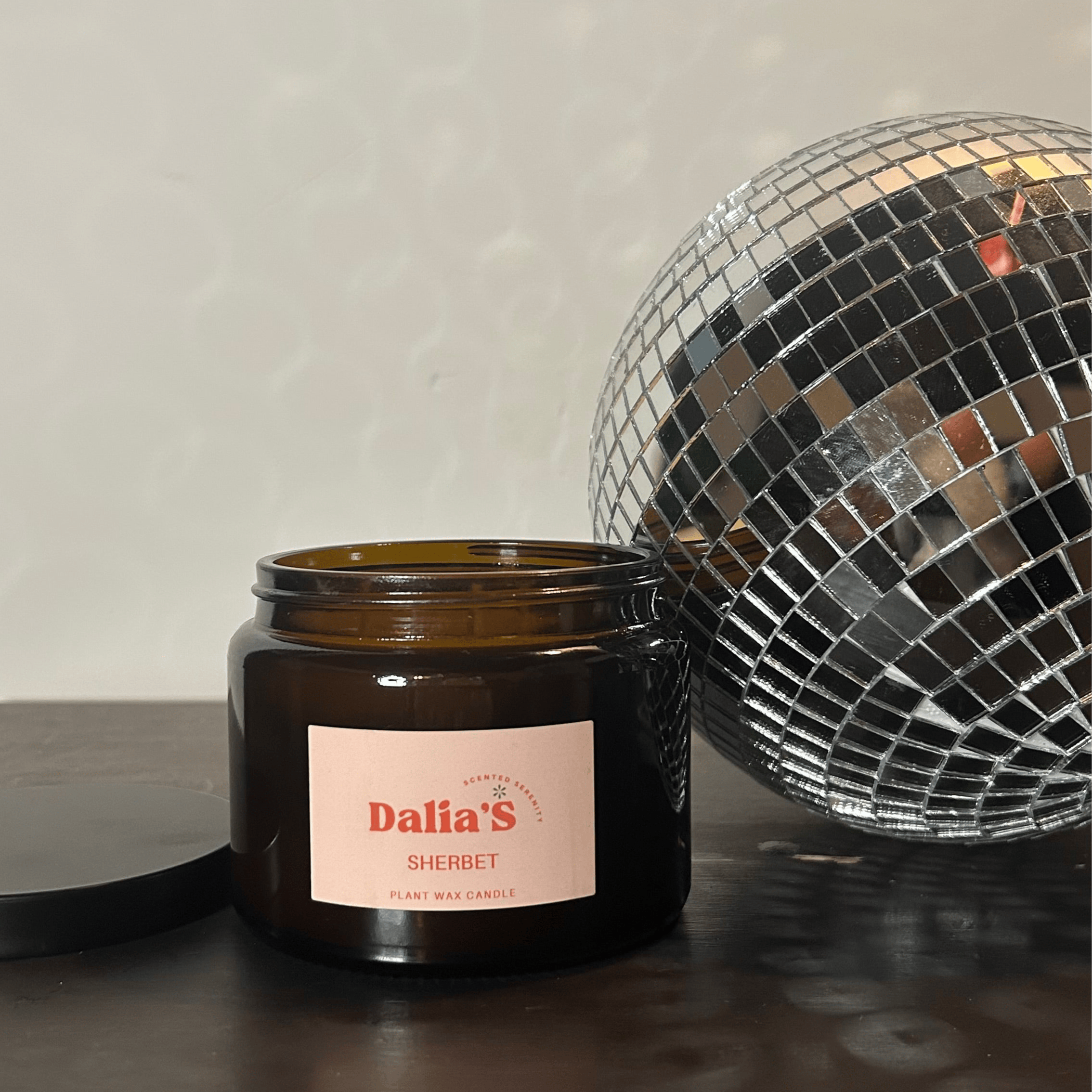 A 500ml brown glass jar 3-wick candle with a label, beside a disco ball.