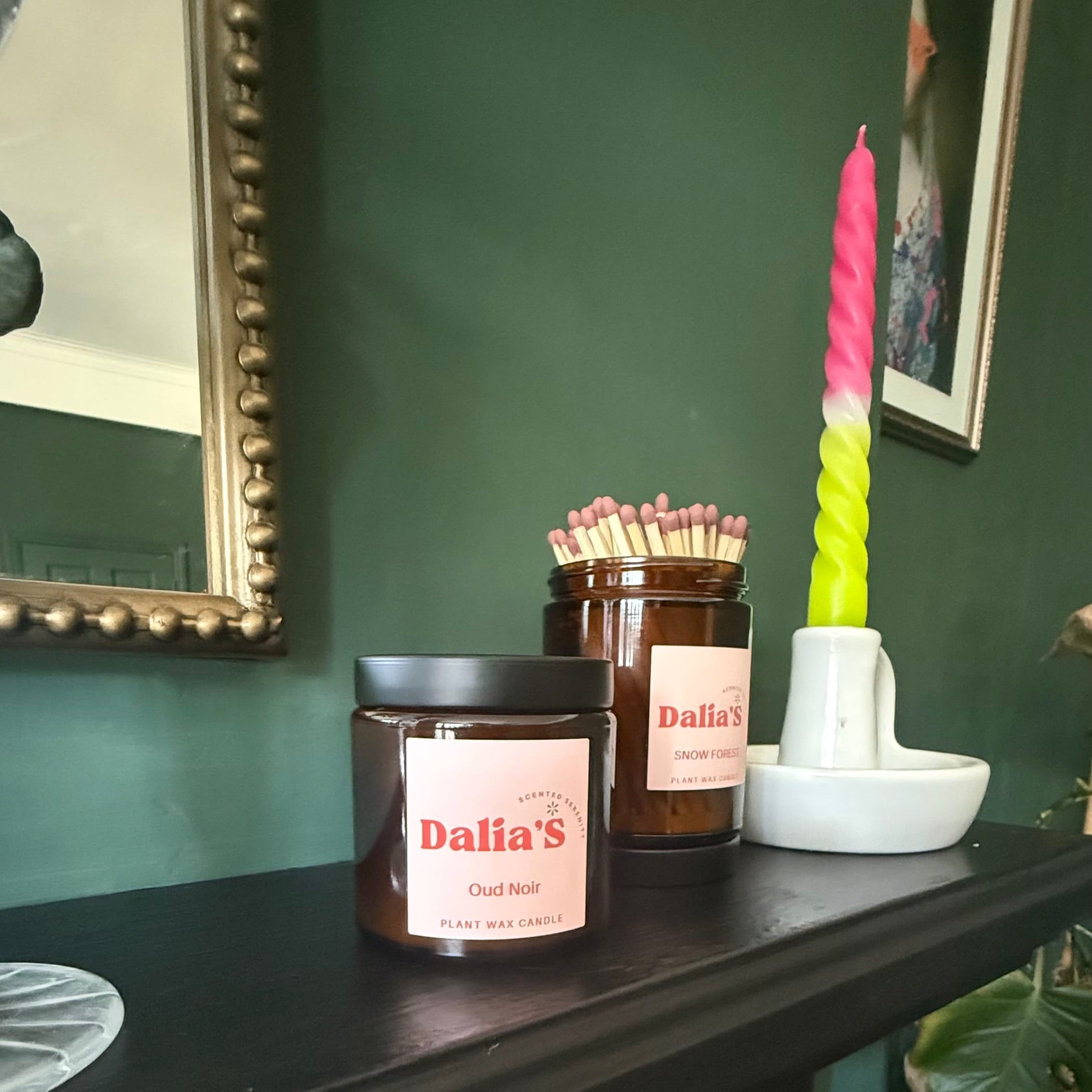 Candles on a dark surface with a green wall and framed picture in the background