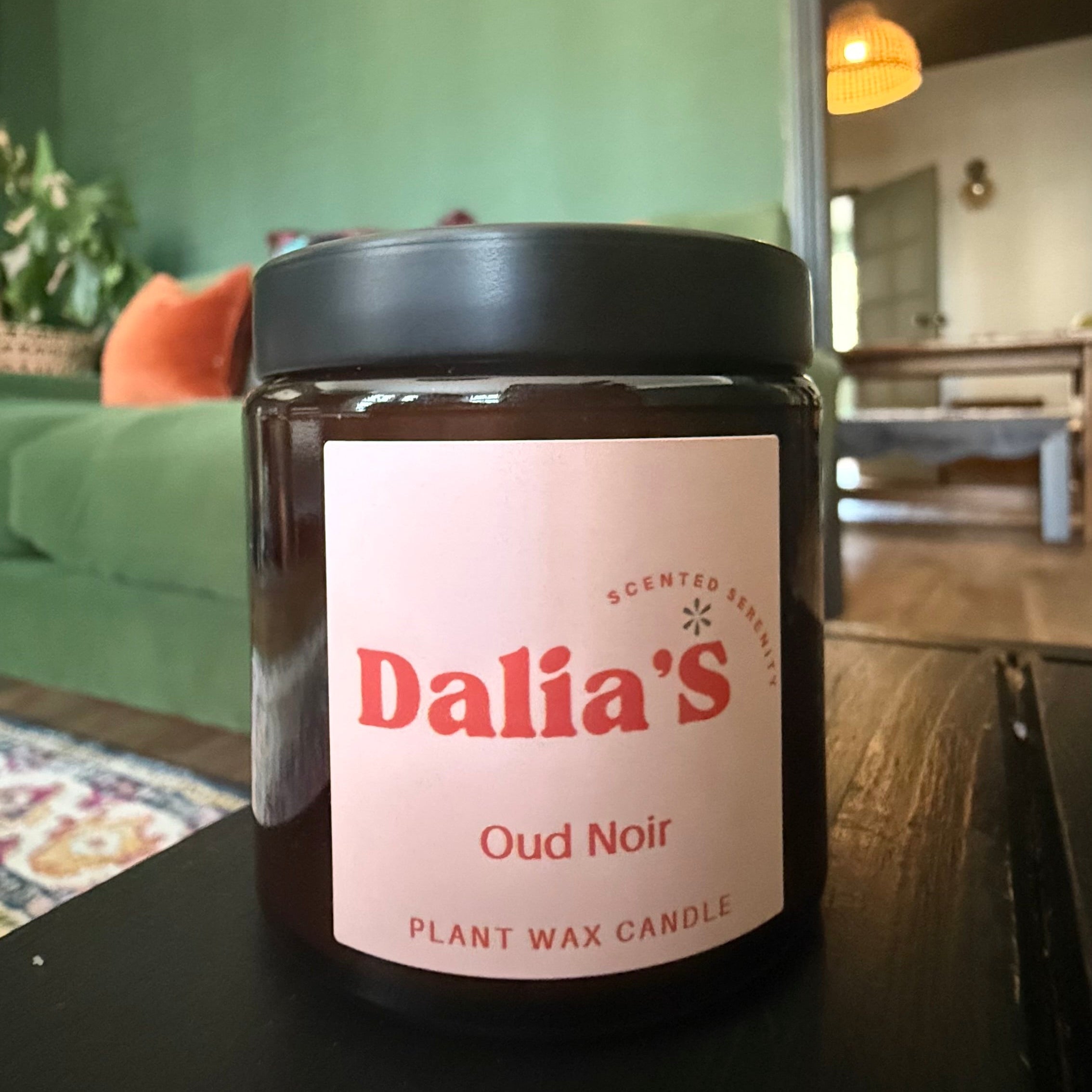 Jar of Dalia's Oud Noir candle on a table with a home interior background