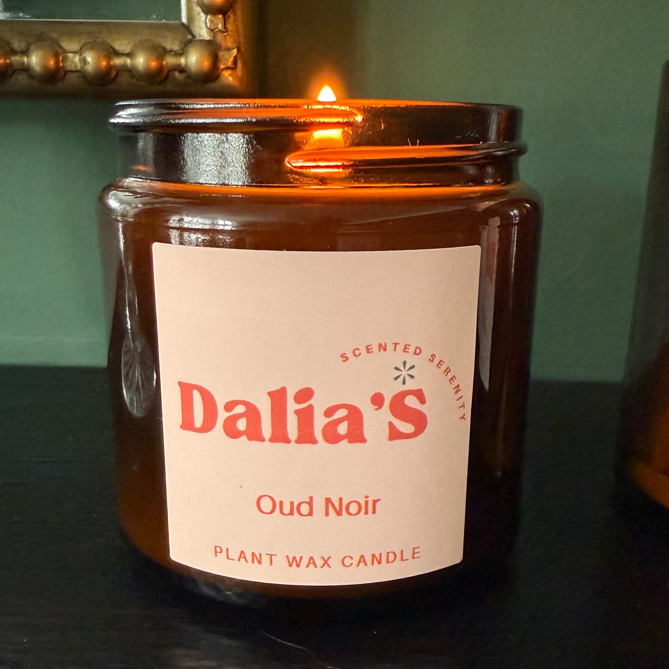 Candle in an amber jar labeled 'Dalia's Oud Noir' on a dark surface.