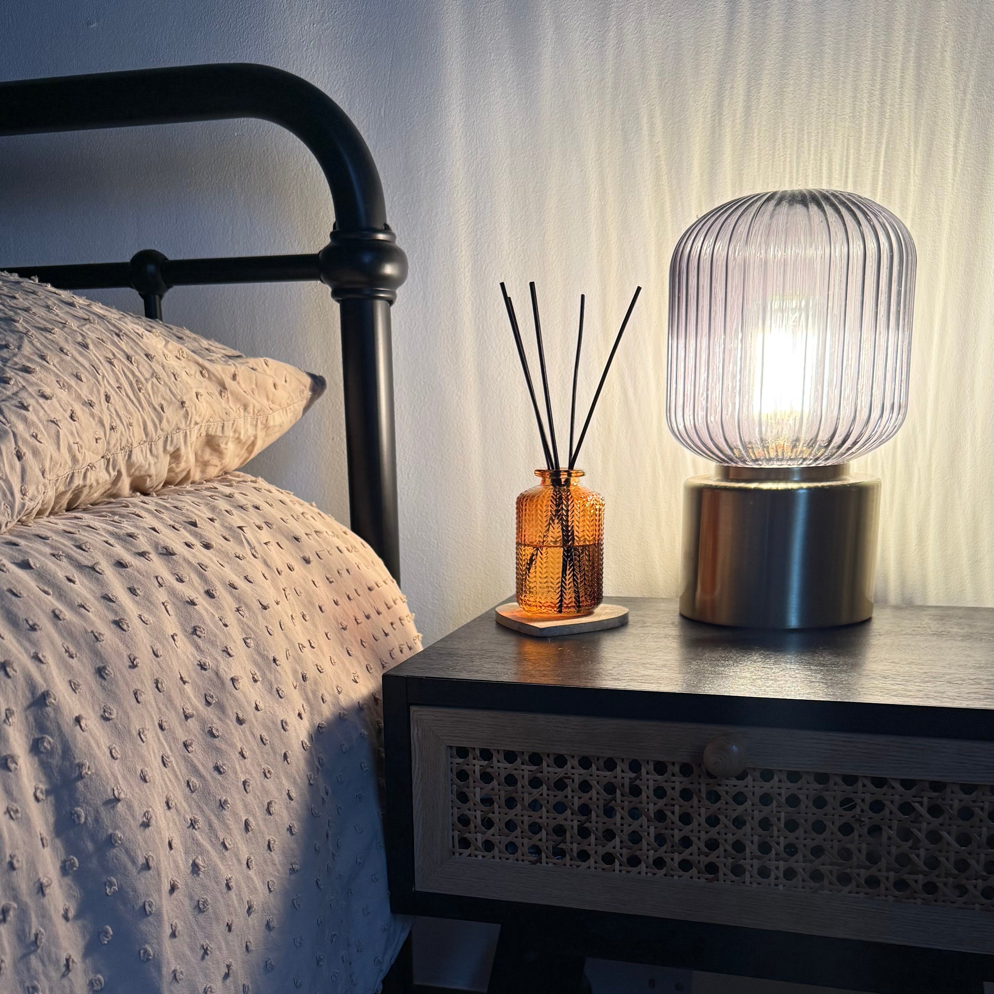 Nighstand with lamp and decorative items next to a bed in a dimly lit room.