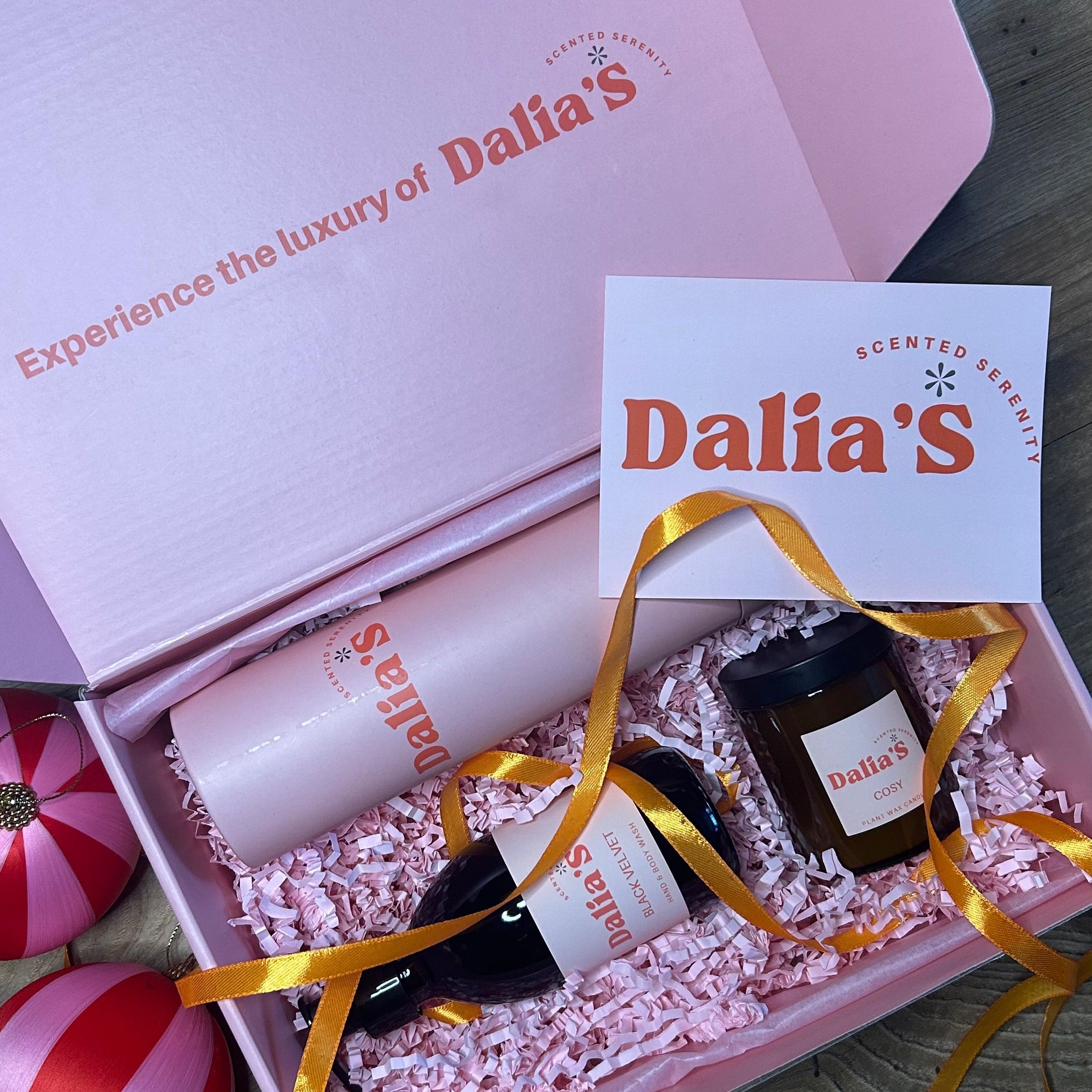 An gift box containing a candle, body wash, and a diffuser from Dalia's brand, all arranged on white paper with a decorative ribbon.