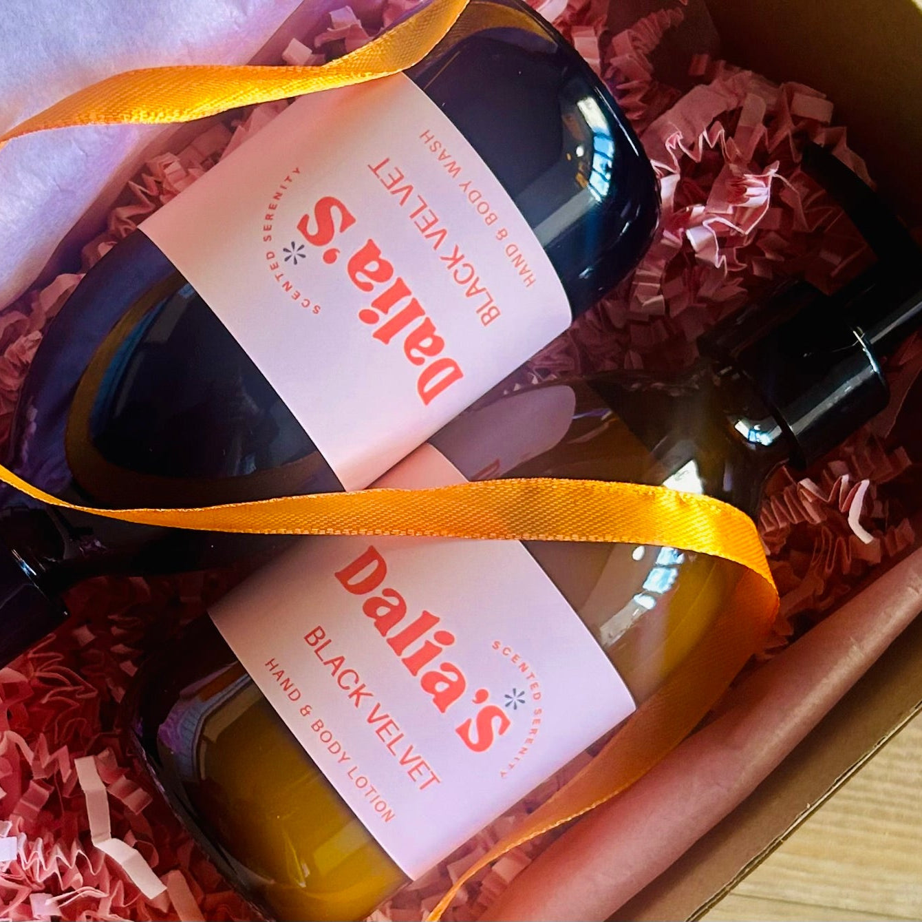 A gift set containing a black velvet hand and body wash and lotion, with bottles adorned with pink labels and sitting in a matching black box with an orange ribbon.