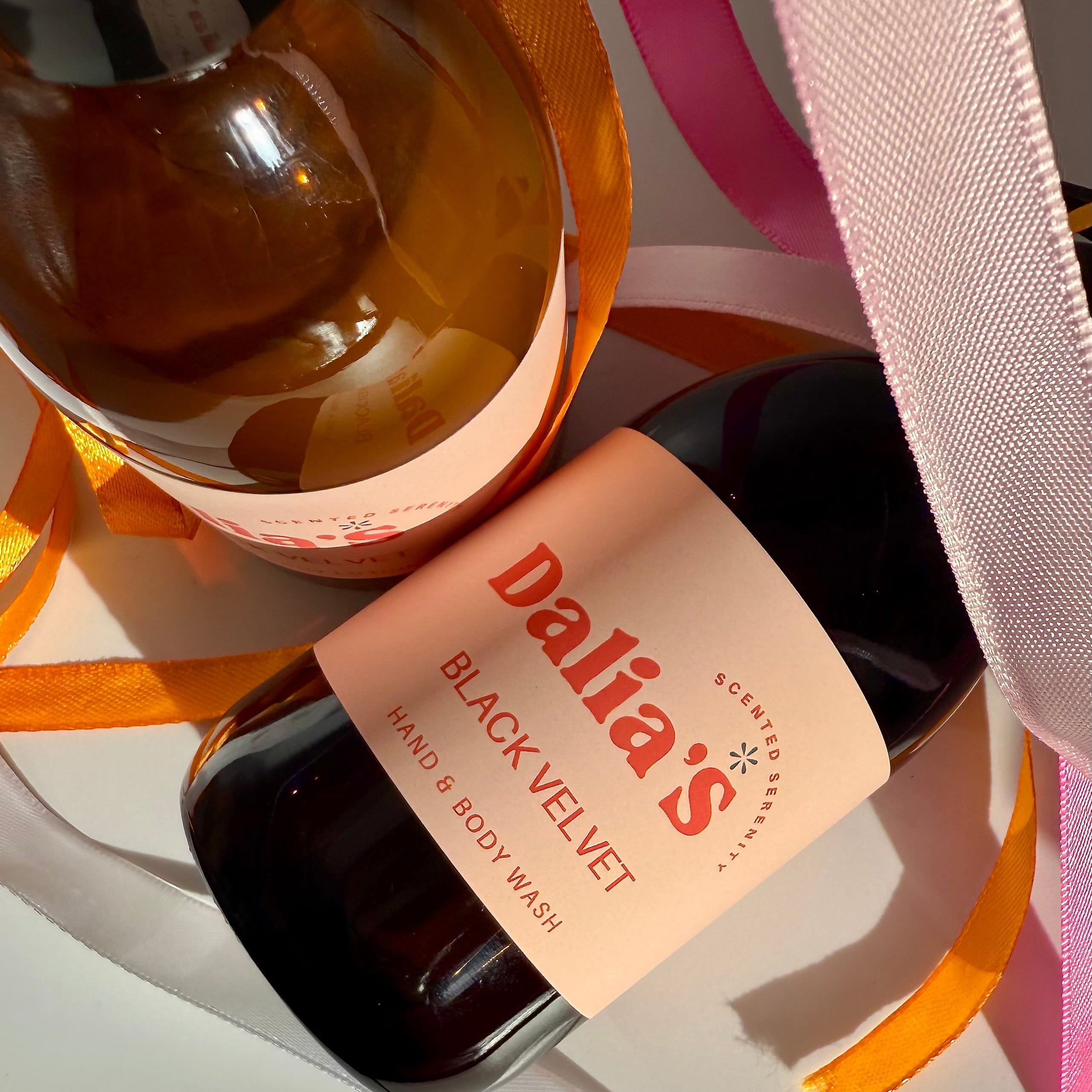 Two bottles of Black Velvet hand and body care products from Dalia's, one for hand wash and one for lotion, with pink and orange ribbons.
